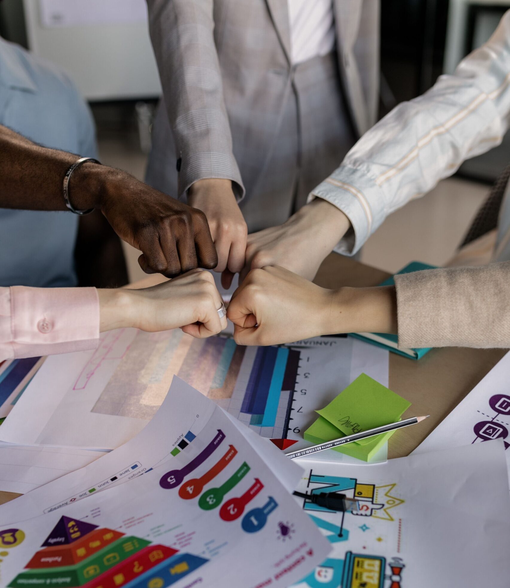A group collaborates with a fist bump over colorful marketing charts, showcasing teamwork.